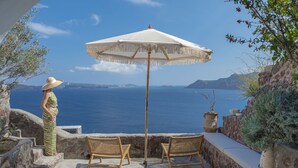 A balcony with wicker chairs, a white umbrella, and a person standing. - Oia Waves by SV (Santorini)