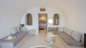 A modern living room with a curved ceiling, a sofa set, a small round table, and a hanging light fixture. - Oia Waves by SV (Santorini)