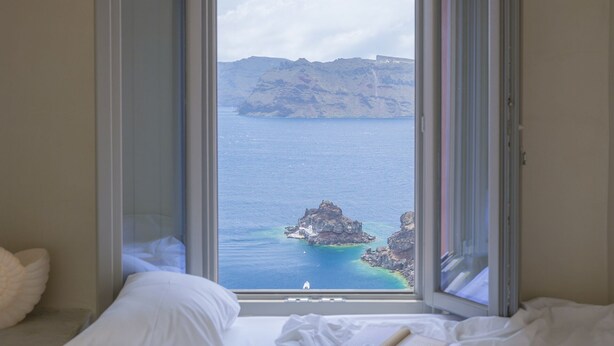 A bedroom with a large window overlooking a coastal view. - Oia Waves by SV (Santorini)