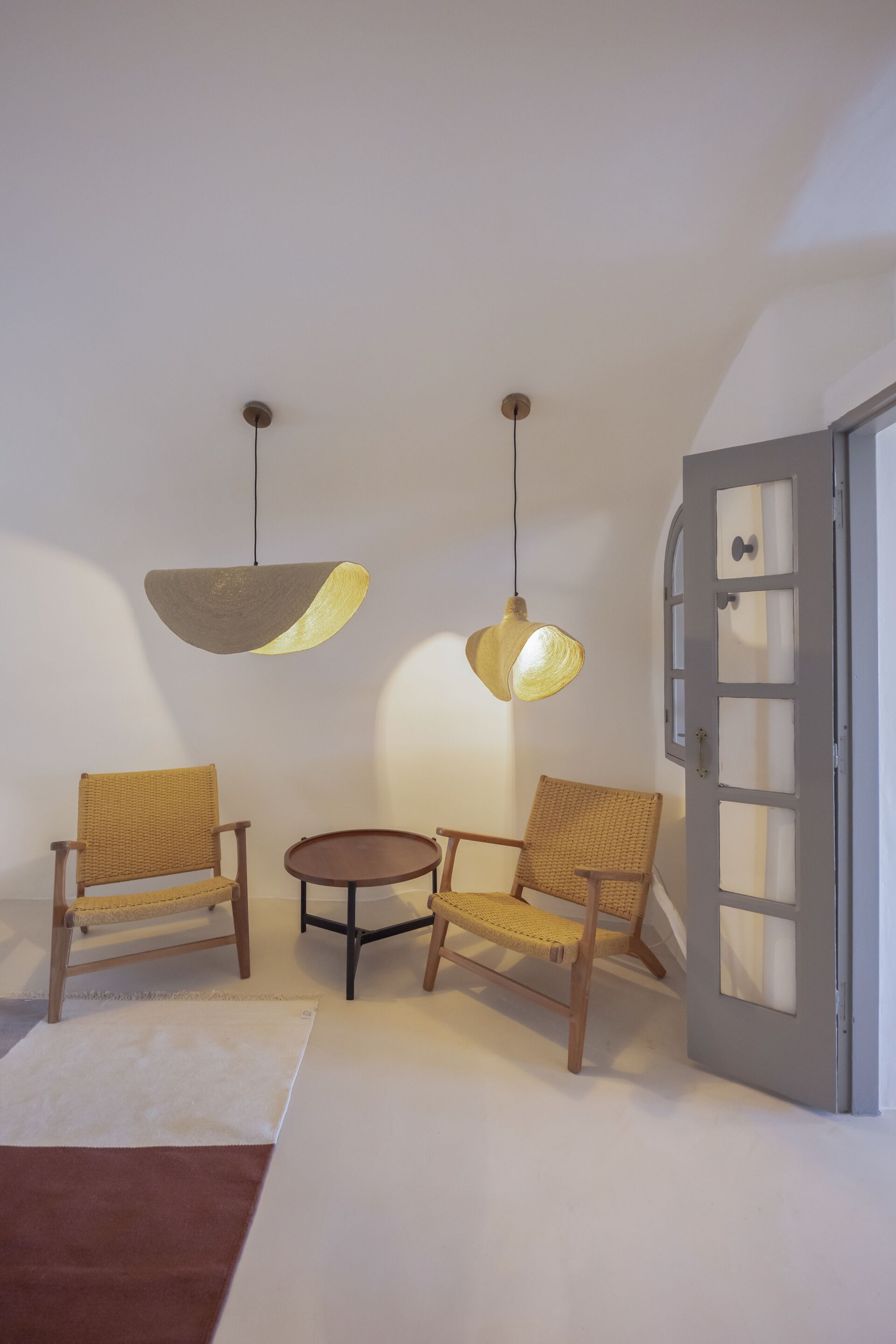 Ein Zimmer mit zwei Korbstühlen, einem kleinen runden Tisch und einer Tür mit satinierten Glasfeldern.
