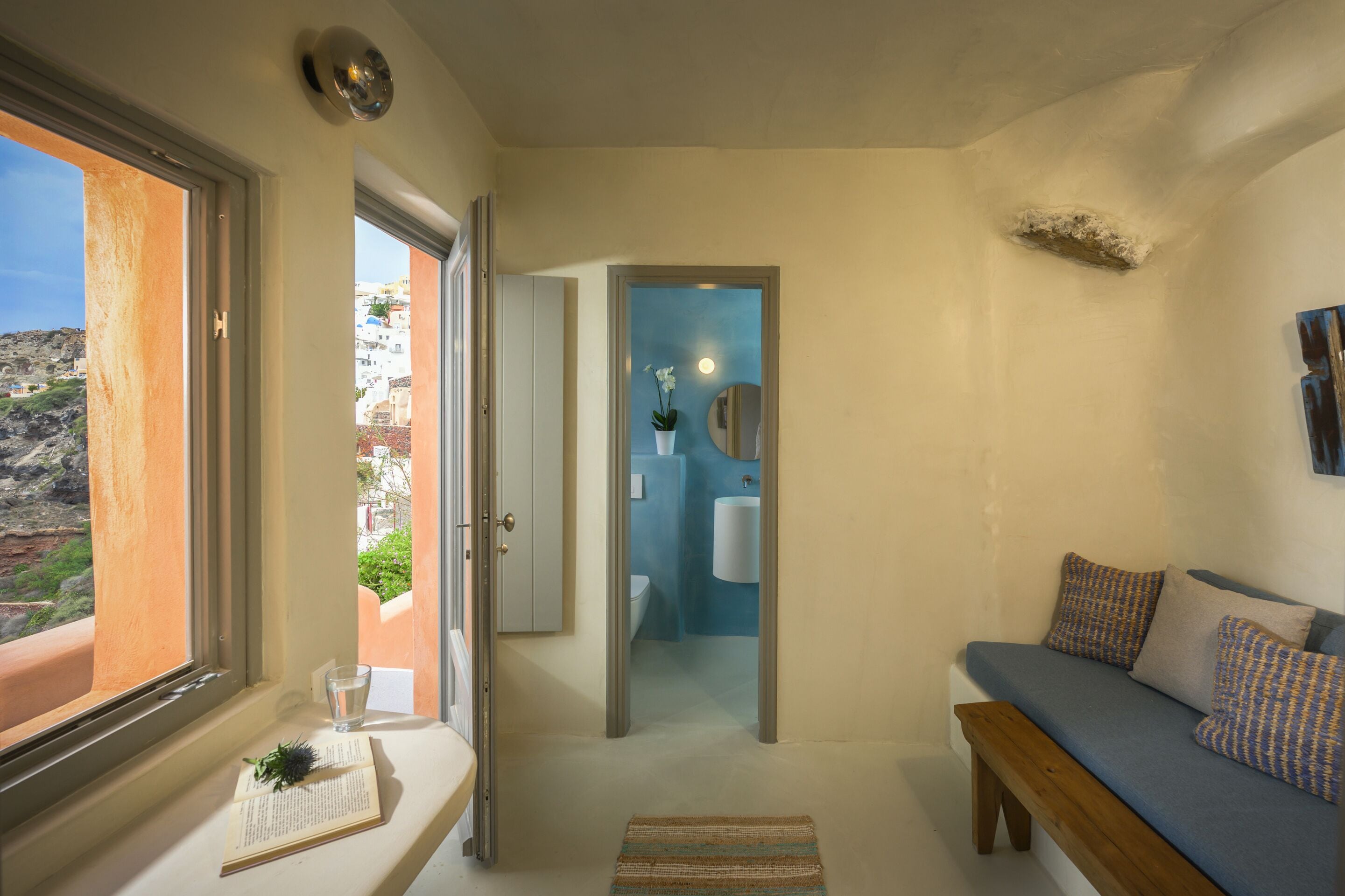 A compact room with a view of a mountainous landscape through a window, a small seating area with a bench, and a bathroom with a blue accent wall.
