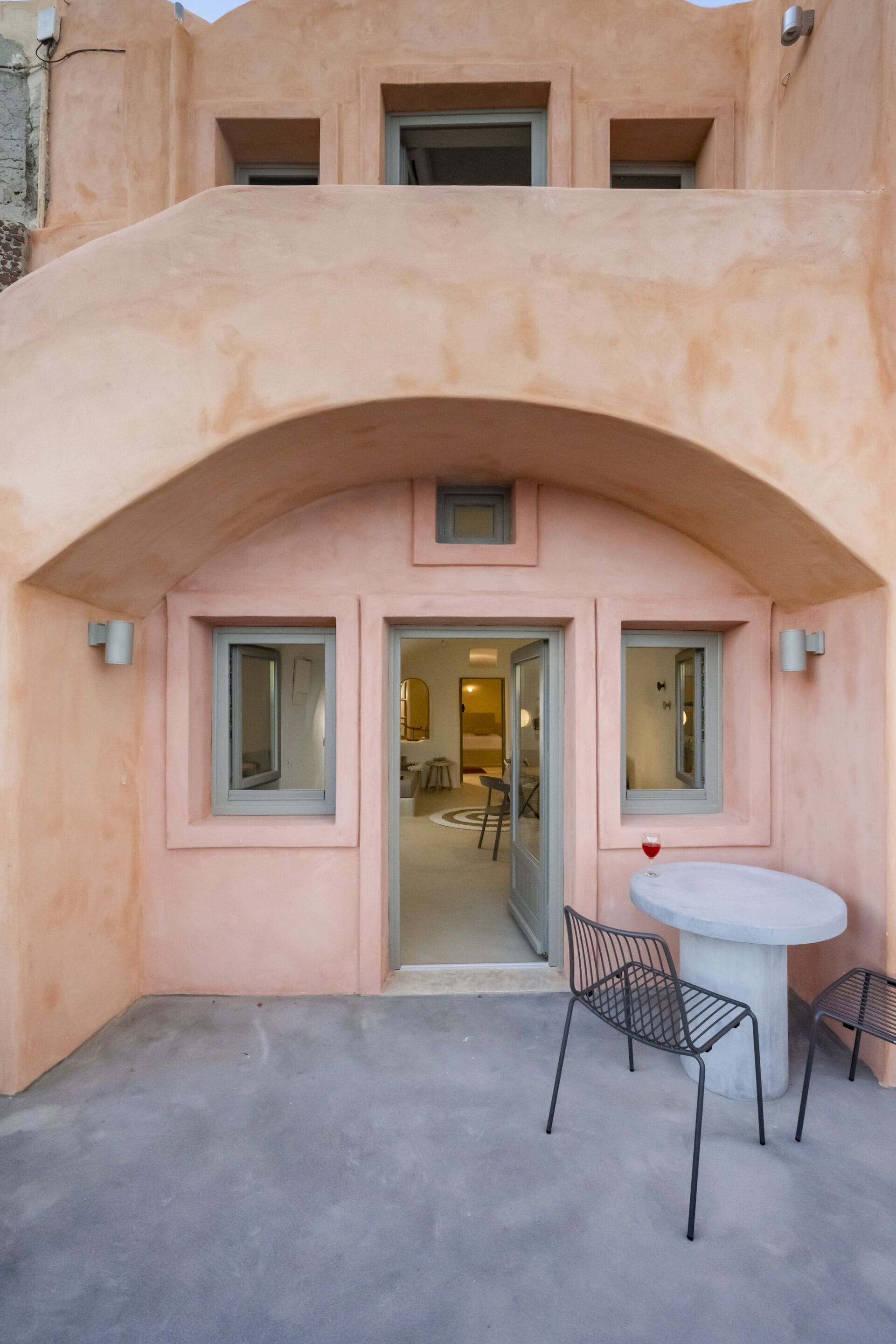 A building with a pink facade, an arched entrance, and a small patio with a table and chairs.