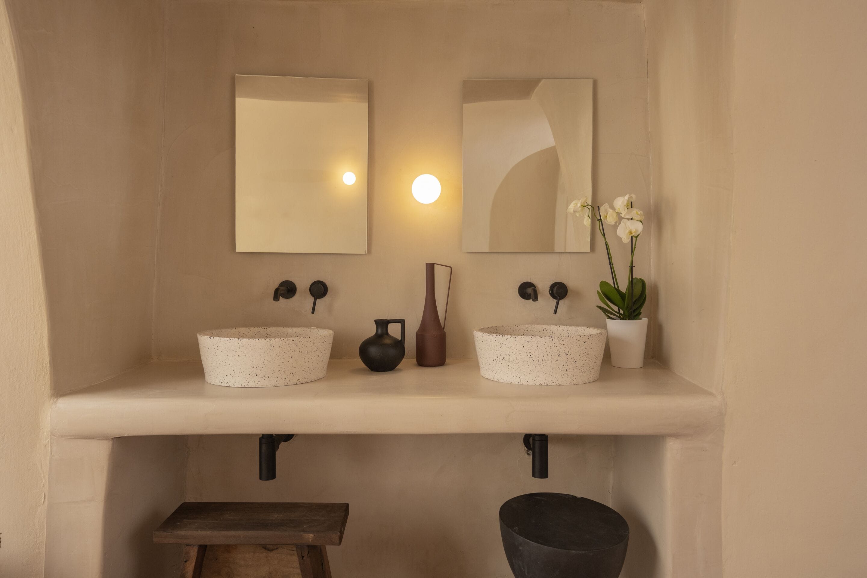 Une salle de bain avec deux lavabos, un miroir, un luminaire et une petite table sur laquelle est posée une plante.