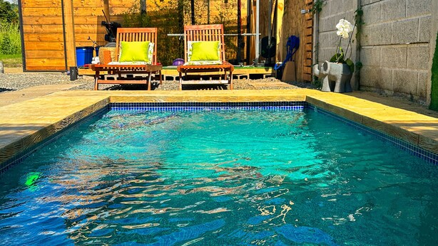 A swimming pool with clear blue water, two wooden lounge chairs with green cushions, and a wooden pergola structure. - Casa Shaka Jaco with Pool Gym Kitchen  (Jacó)