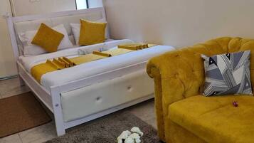 Un dormitorio con cama, sofá, una mesita con un florero y mando a distancia, y una lámpara de pared.
