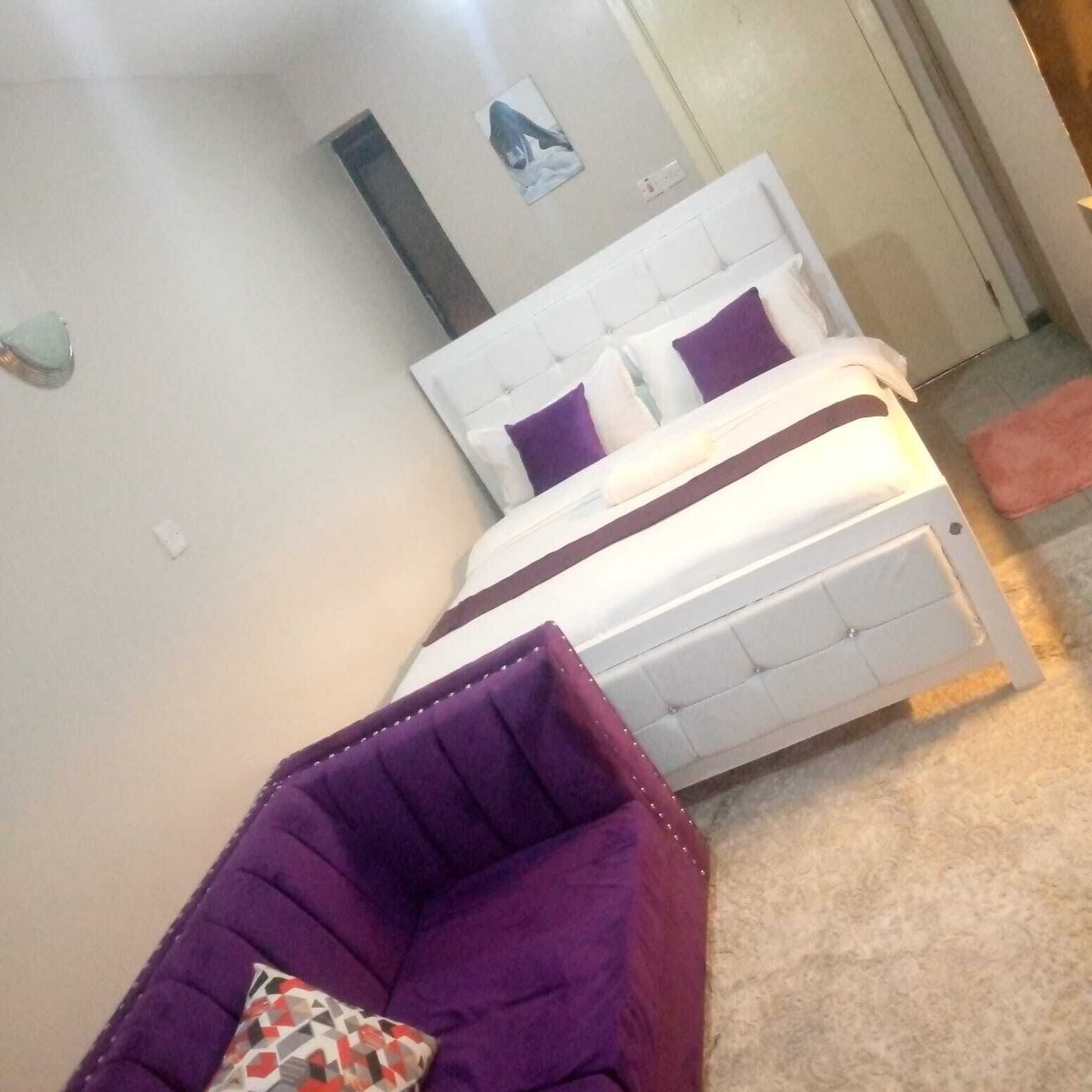 A bedroom with a bed, a purple chair, and a small rug.