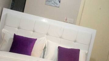 Una cama con cabecera blanca y dos almohadas moradas.