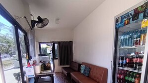 A compact room with a wooden floor, a sofa, a small table, a refrigerator stocked with beverages, and a window providing a view of the outside. - The Loftel Resort (Bangkok)