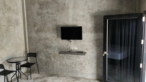 A room with a flat-screen TV mounted on the wall, a small table with two chairs, and a sliding door.