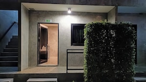 A modern building entrance with a sign indicating room B2, a staircase to the left, and a large hedge to the right. - The Loftel Resort (Bangkok)