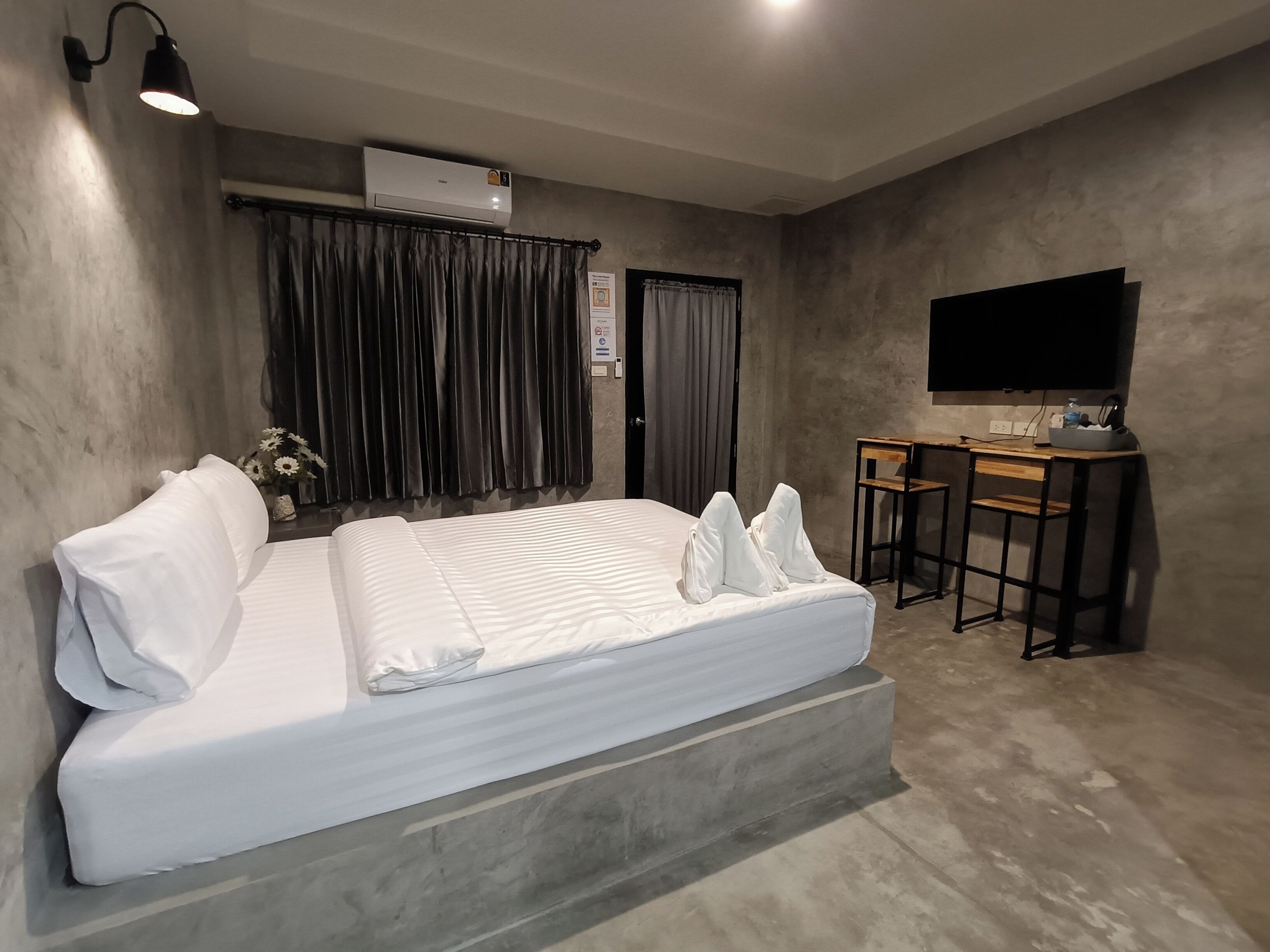 A modern hotel room with a large bed, a desk, a flat-screen TV, and an air conditioning unit.