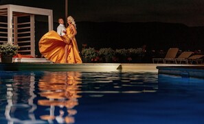 A couple by a pool with a white structure and lounge chairs in the background. - Riviera by Queens (Drobeta-Turnu Severin)