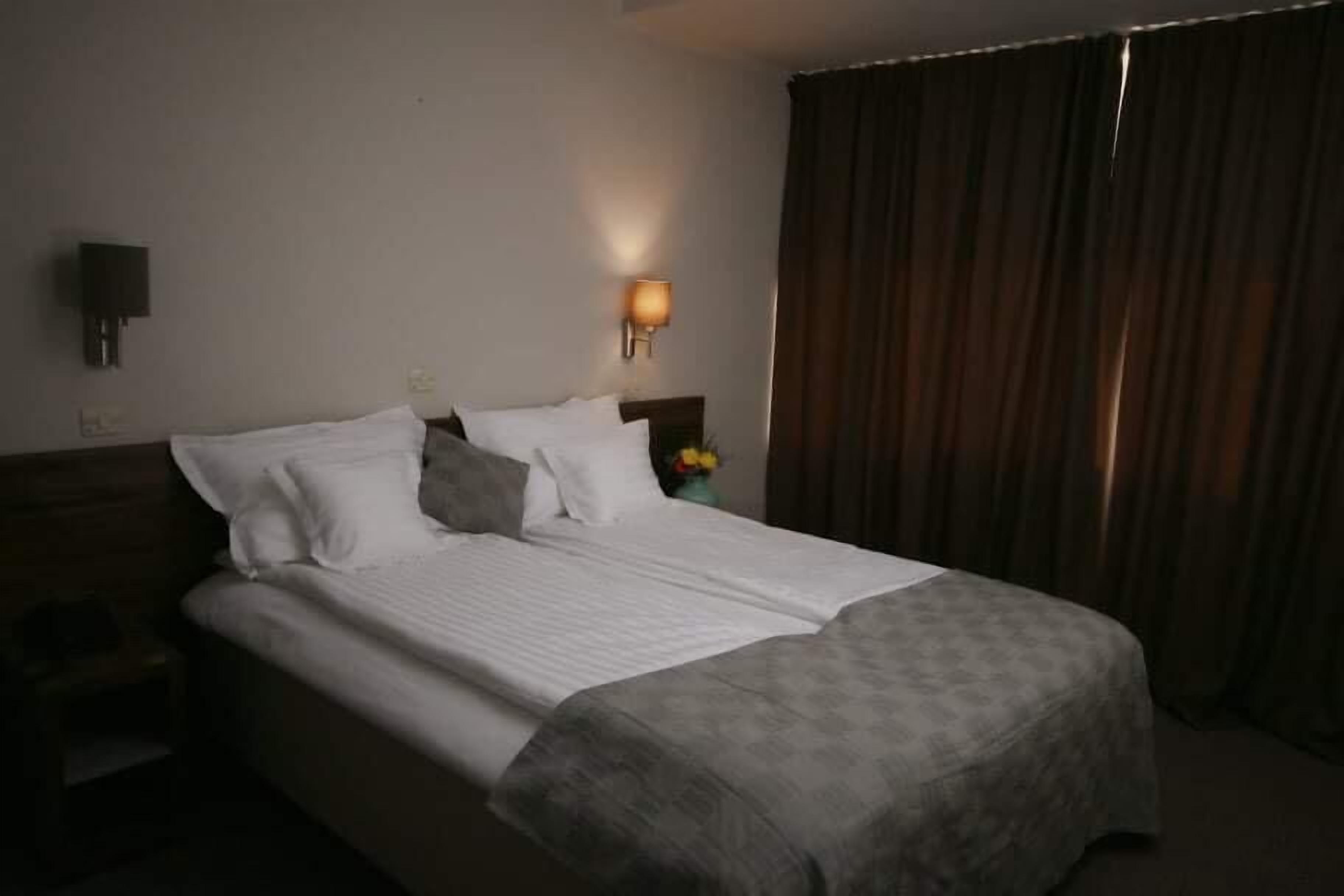 A hotel room with a bed, a nightstand, a lamp, and a curtain.