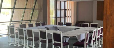 Un salón de conferencias con una larga mesa y sillas, ventanas amplias y un diseño moderno en el techo.