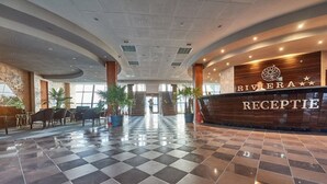 A hotel reception area with a checkered floor, a reception desk, and a staircase leading to upper floors. - Riviera by Queens (Drobeta-Turnu Severin)
