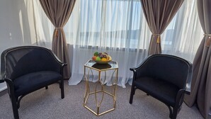 A room with two black chairs, a small round table with a fruit bowl, and sheer curtains. - Riviera by Queens (Drobeta-Turnu Severin)