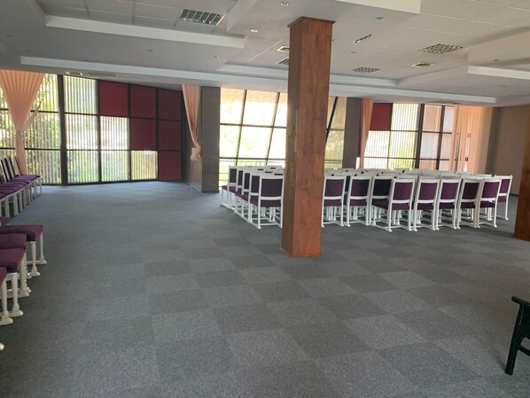 A spacious room with rows of white chairs and purple cushions, large windows with blinds, and a grey carpeted floor. - Riviera by Queens (Drobeta-Turnu Severin)