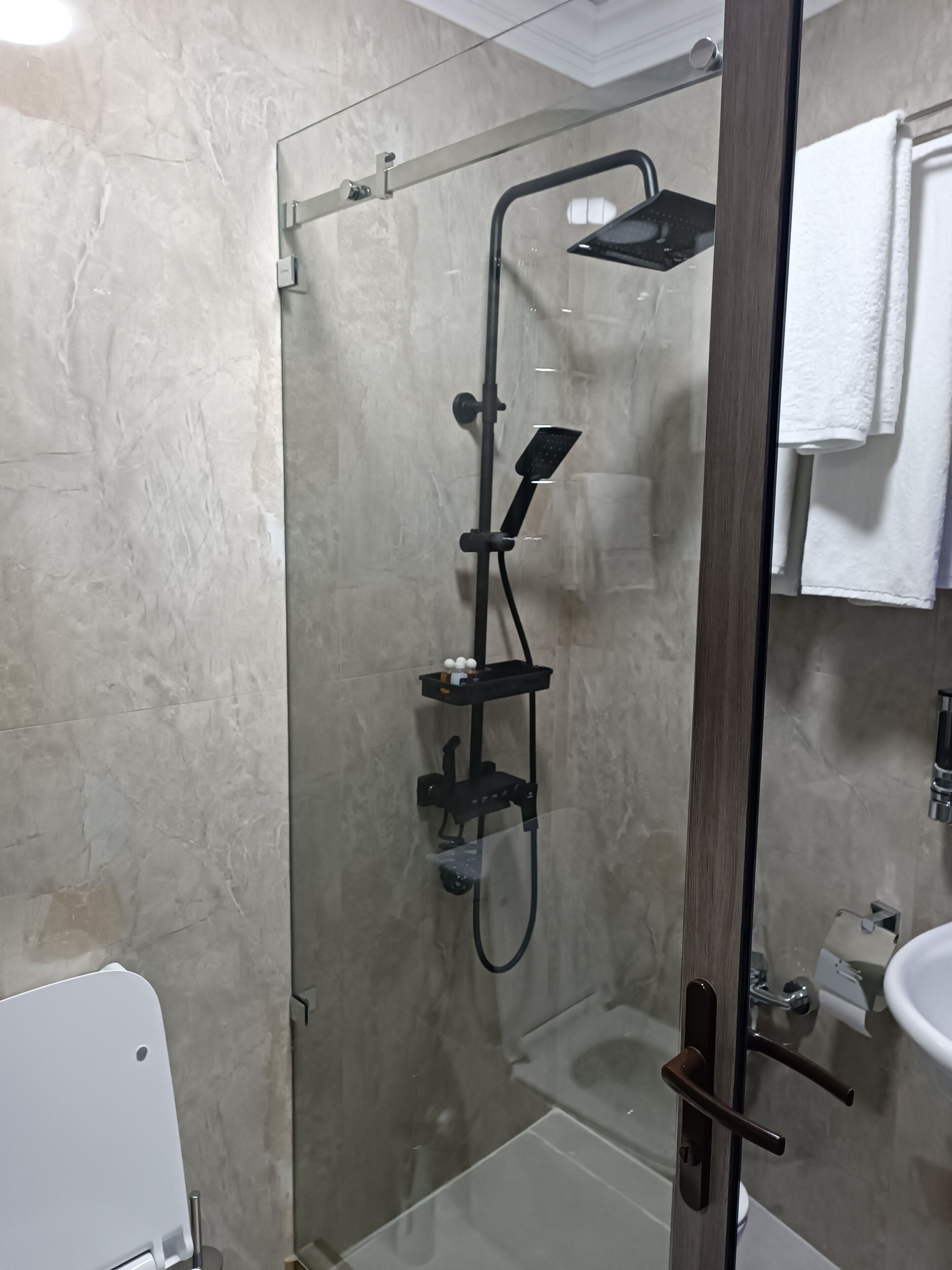 Una ducha con cerramiento de vidrio, con un cabezal de ducha de mano y un grifo empotrado.