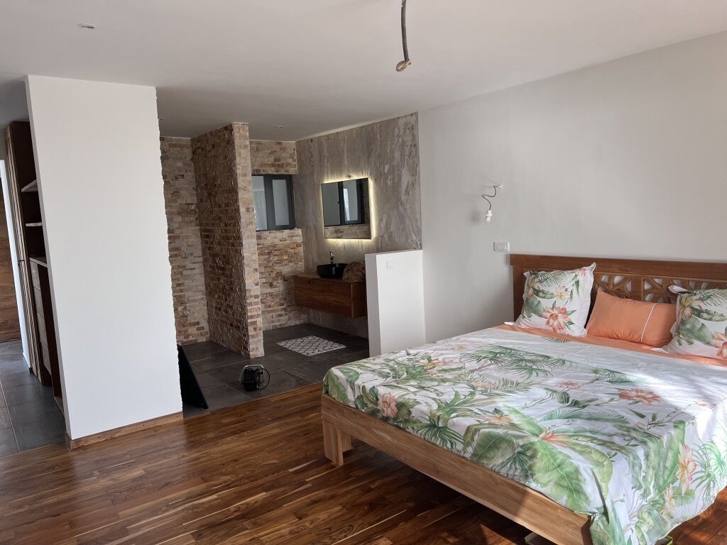 Une chambre avec un lit en bois, un mur en briques, une petite salle de bain et une armoire blanche.