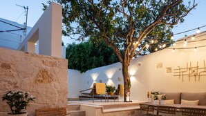 A modern outdoor patio with a stone wall, a tree, and a dining area with chairs and a table. - Modern Stone Villa Lemonia w/(heated-hot tub)pool/Steam room, Old City, Rethymno (Rethymno)