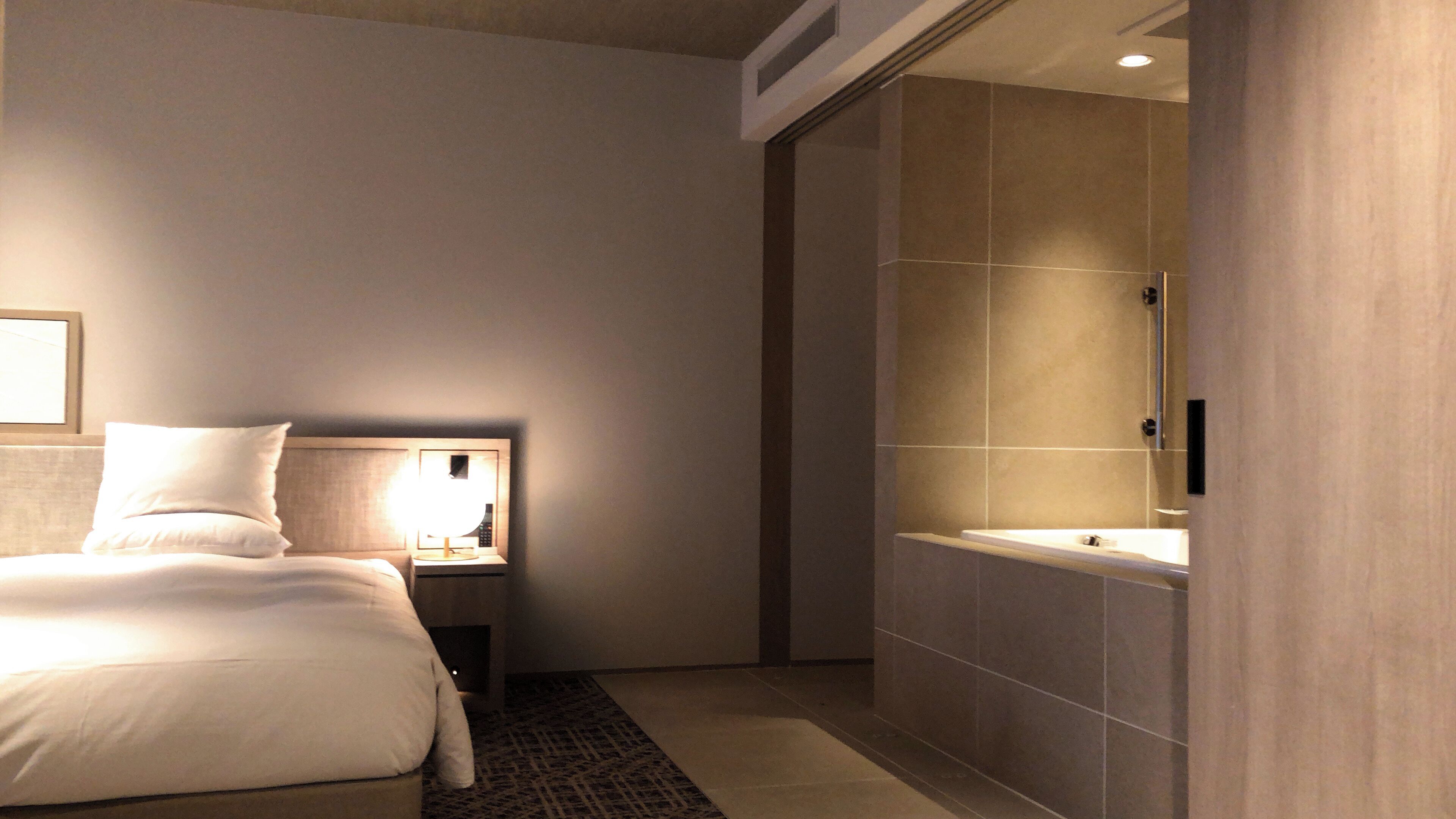 Una habitación de hotel moderna con cama, mesita de noche, lámpara y un espejo grande.