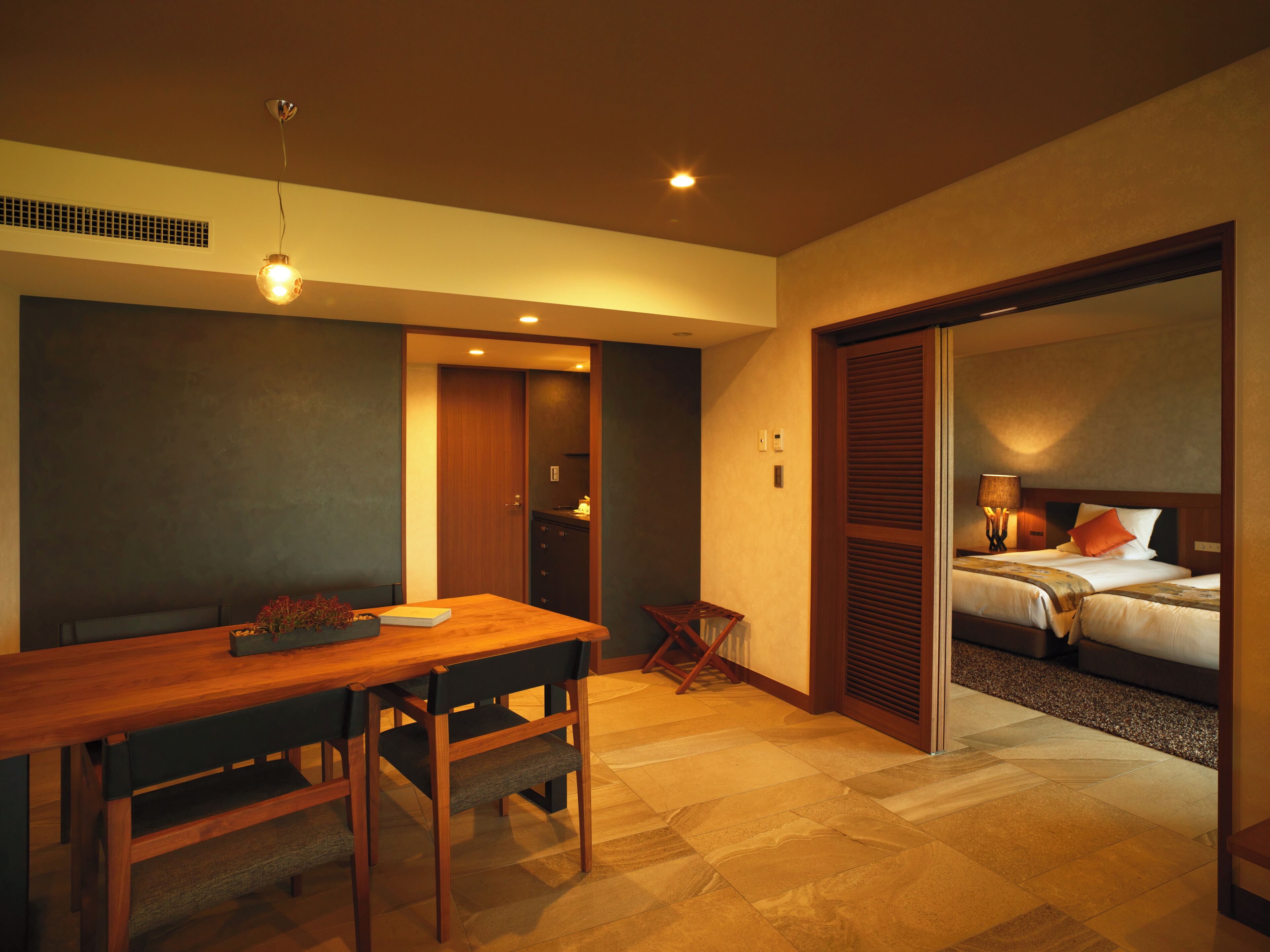 A hotel room with a wooden dining table, a bed with a headboard, and a small seating area.