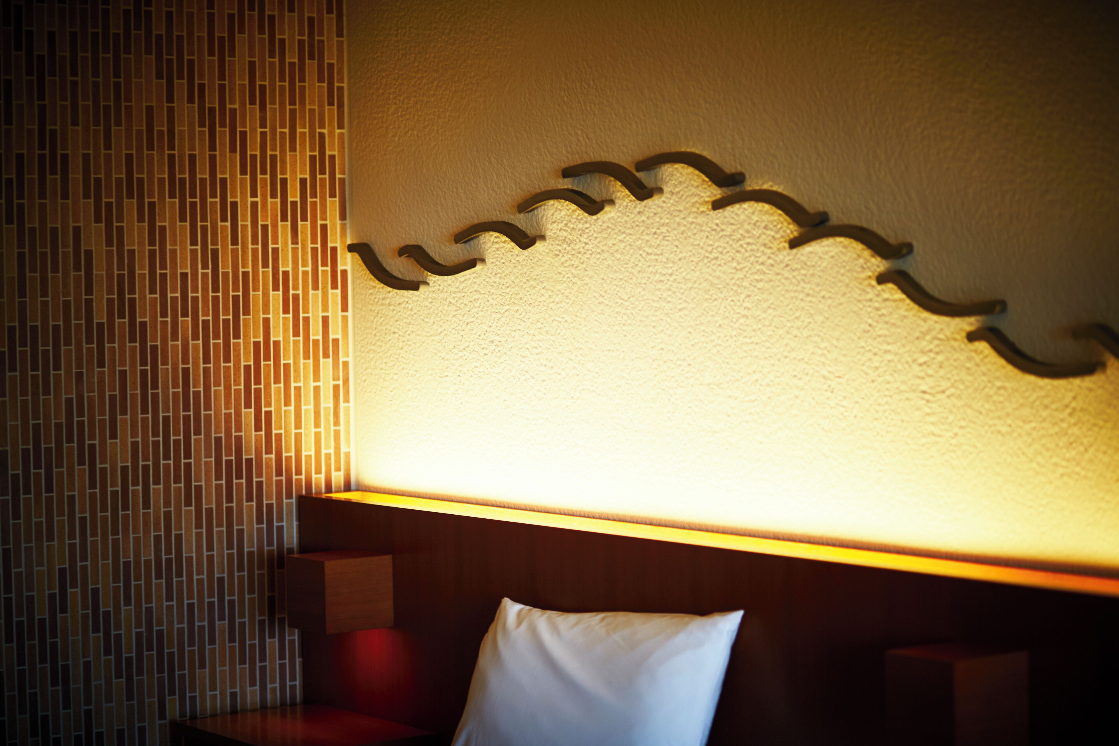 Ett hotellrum med en vägg som har en intressant yta, en sänggavel i trä och en vit kudde.