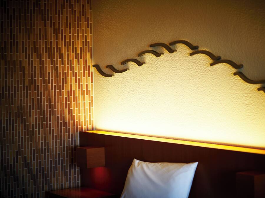A hotel room with a textured wall, a wooden headboard, and a white pillow.