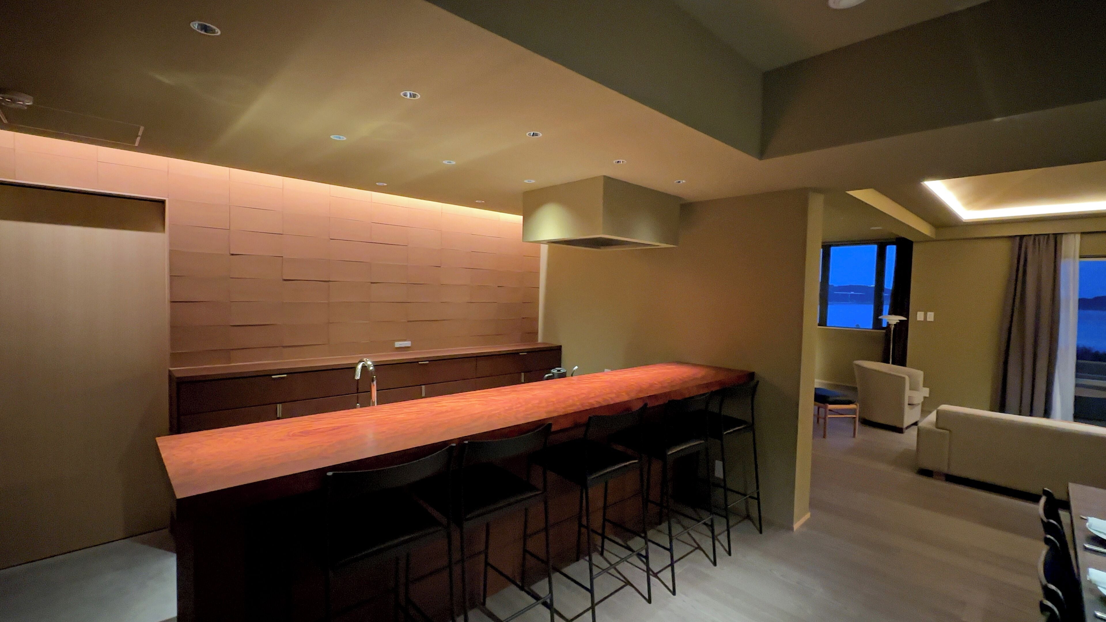 Una cocina moderna con una encimera larga, taburetes de bar y un horno empotrado.