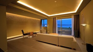 A modern hotel room with a large sofa, a dining table, and chairs. There is a large window with a view of the outdoors. - Hotel Anaga (Minamiawaji)