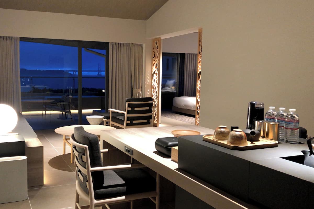 Ett modernt hotellrum med ett stort fönster, ett skrivbord, en soffa och en matplats.