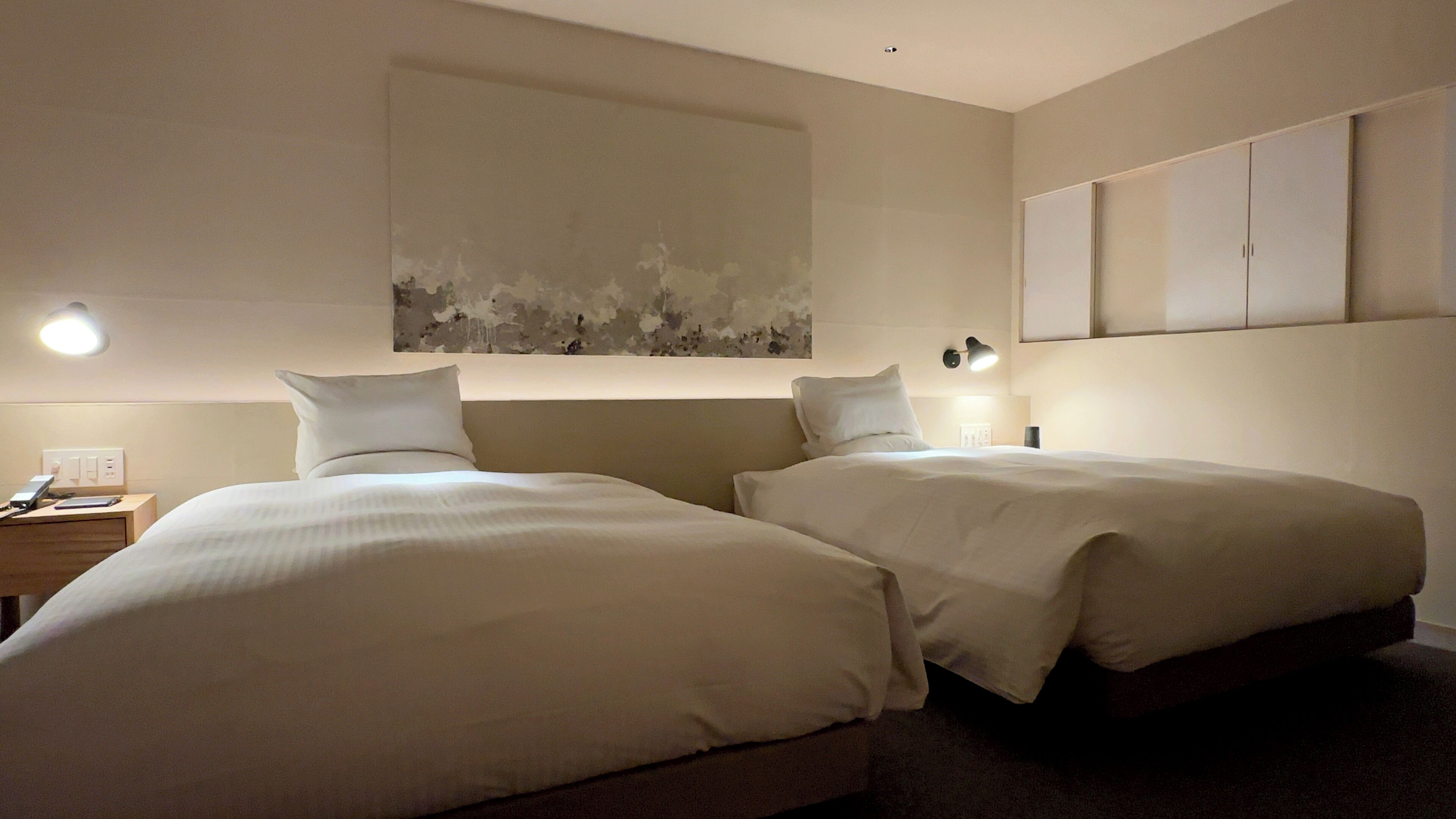 A hotel room with two beds, a nightstand, a lamp, and a painting on the wall.