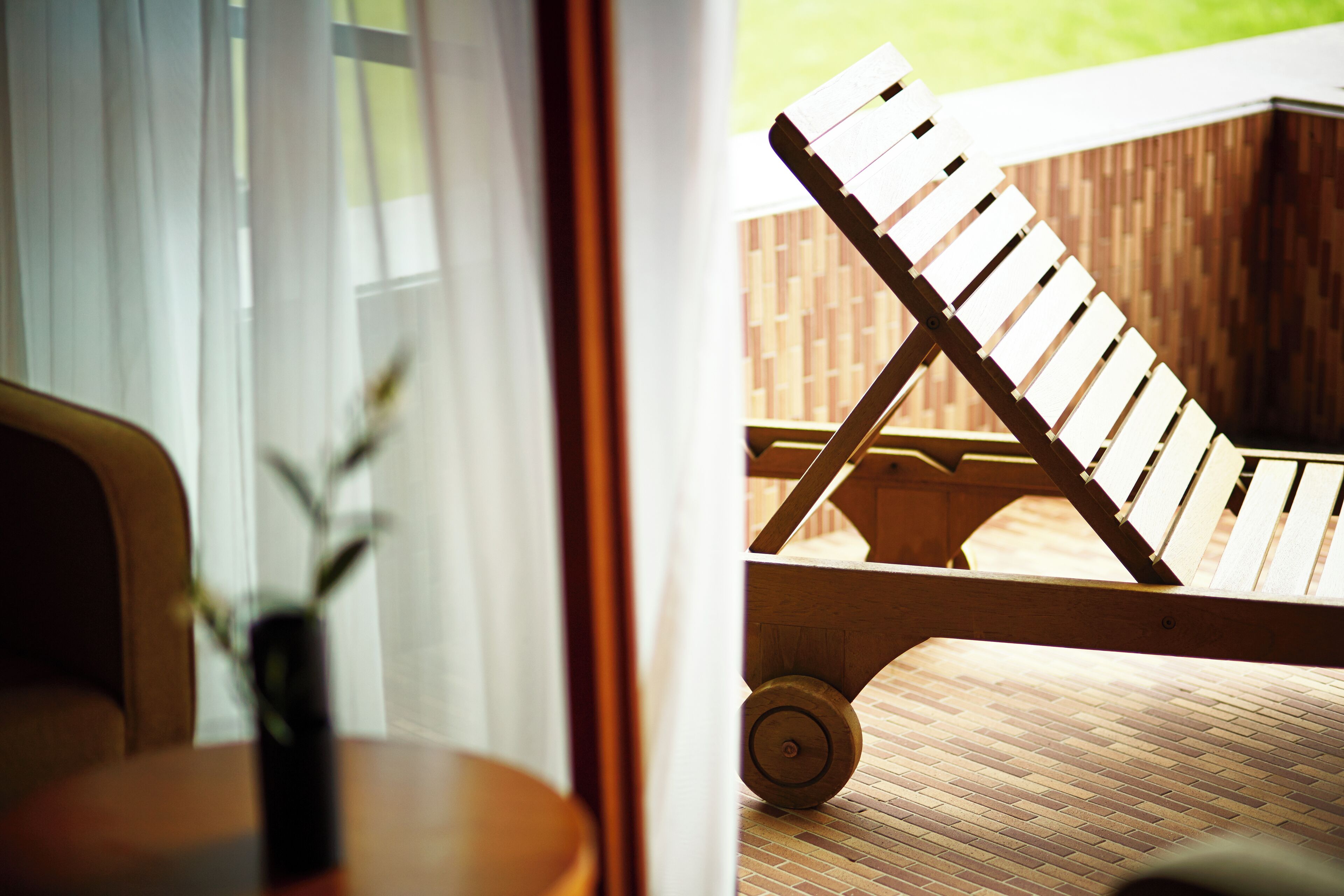 Una silla lounge de madera con diseño de listones, ubicada sobre una terraza de madera con patrón de ladrillo.