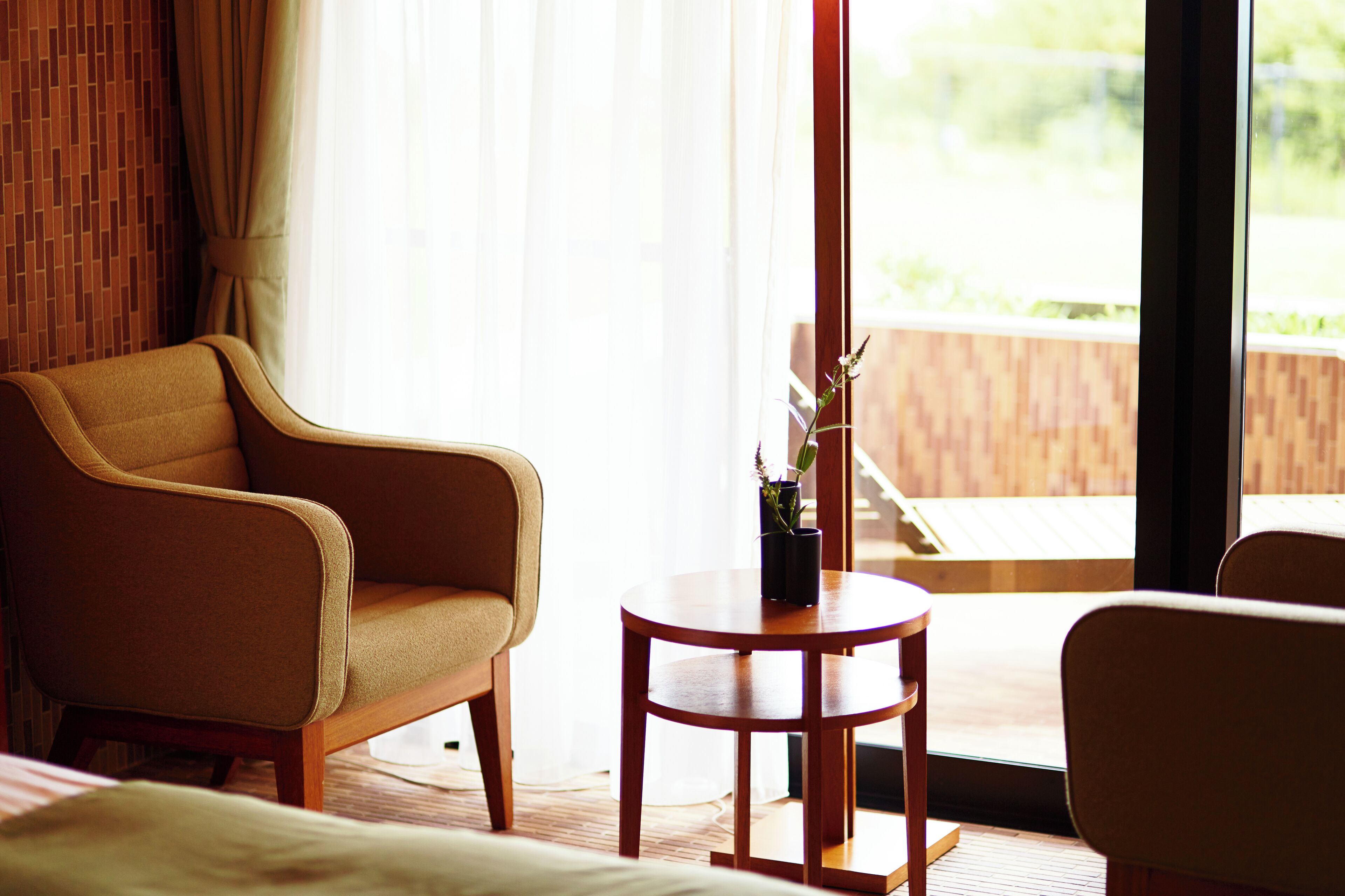A hotel room with a large window, a wooden floor, a round wooden table, and two armchairs.