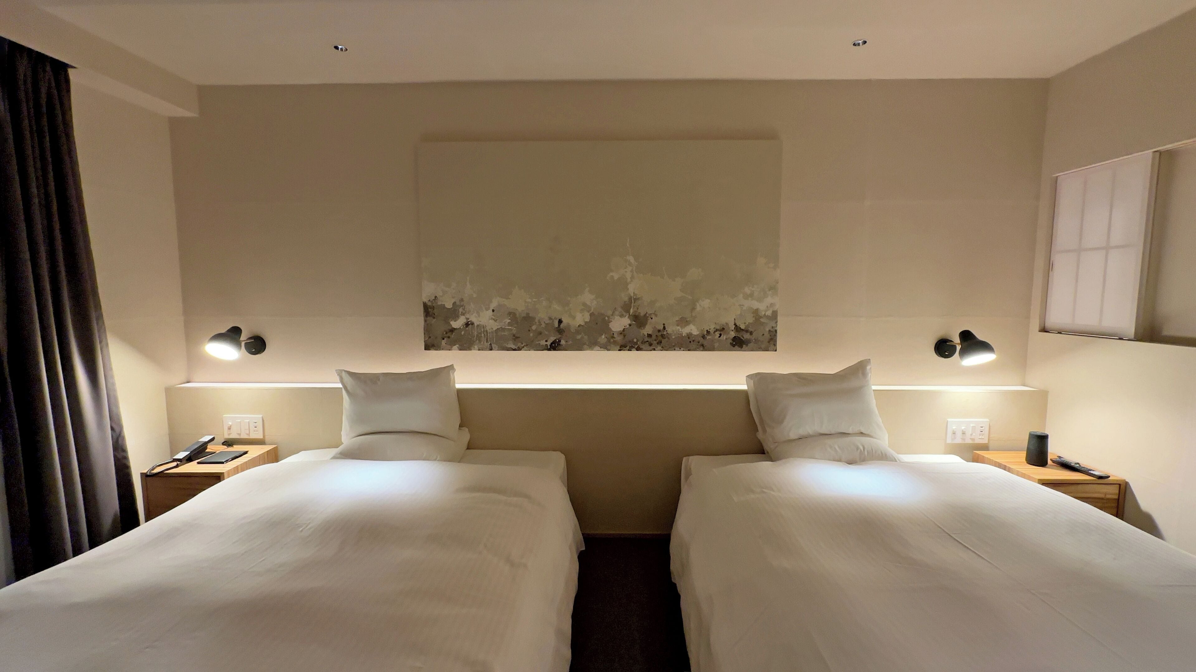 Une chambre d’hôtel avec deux lits simples, une grande peinture abstraite au mur et des lampes de chevet.