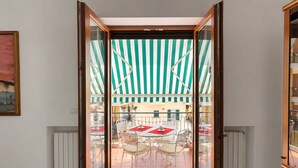 A room with a sliding glass door leading to an outdoor patio with a striped awning, white furniture, and a tiled floor.