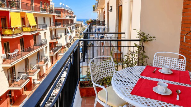 A balcony with white wicker furniture, a red tablecloth, and a view of adjacent buildings.
