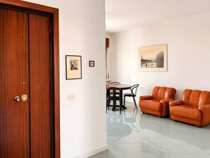 Una habitación con puerta de madera, una mesa de comedor con sillas, un sofá y cuadros en la pared.