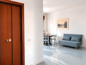 A room with a wooden door, a blue sofa, a dining table with chairs, and a framed picture on the wall.