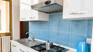 A modern kitchen with white cabinets, a gas stove, a sink, and blue tiles.