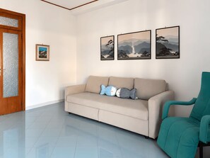 A living room with a beige sofa, a teal armchair, and three framed landscape paintings on the wall. - From Sorrento With Love - Big sea view apartment in center of Sorrento (Sorrento)