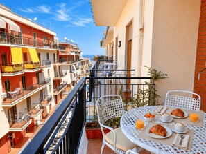 Un balcon avec une table préparée pour le petit-déjeuner, donnant sur une rangée d’immeubles.