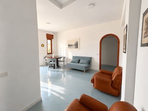 Ampla sala de estar com mesa de jantar, sofá azul e poltronas de couro.