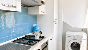 A compact kitchen with a gas stove, a kettle, and a built-in washing machine.