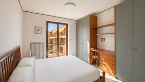 A bedroom with a bed, a wooden wardrobe, a radiator, and a view of a balcony.