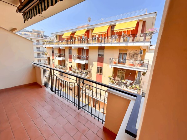 Edifício residencial com várias andares, varandas, plantas em vasos e céu claro.