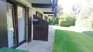 A patio area with a green table, a wooden fence, and a gravel path leading to a grassy lawn. - Ferienwohnung 45 qm, für 2 Personen (Inzell)