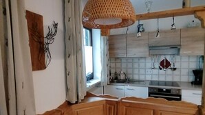 A modern kitchen with wooden cabinetry, a built-in bench, and a hanging pendant light. - Ferienwohnung 45 qm, für 2 Personen (Inzell)