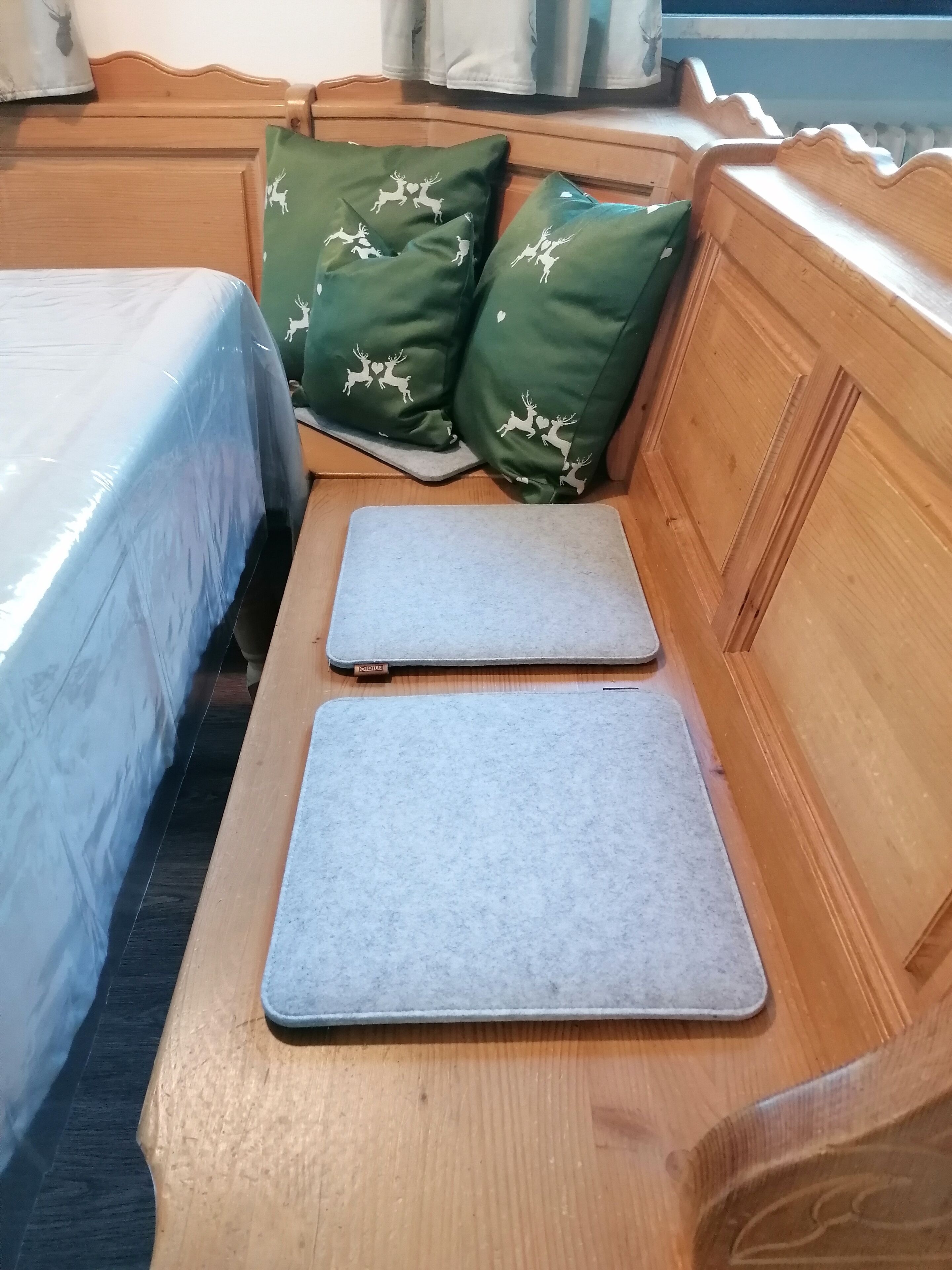 Un banco de madera con dos tapetes grises y almohadones verdes con diseños de ciervos.