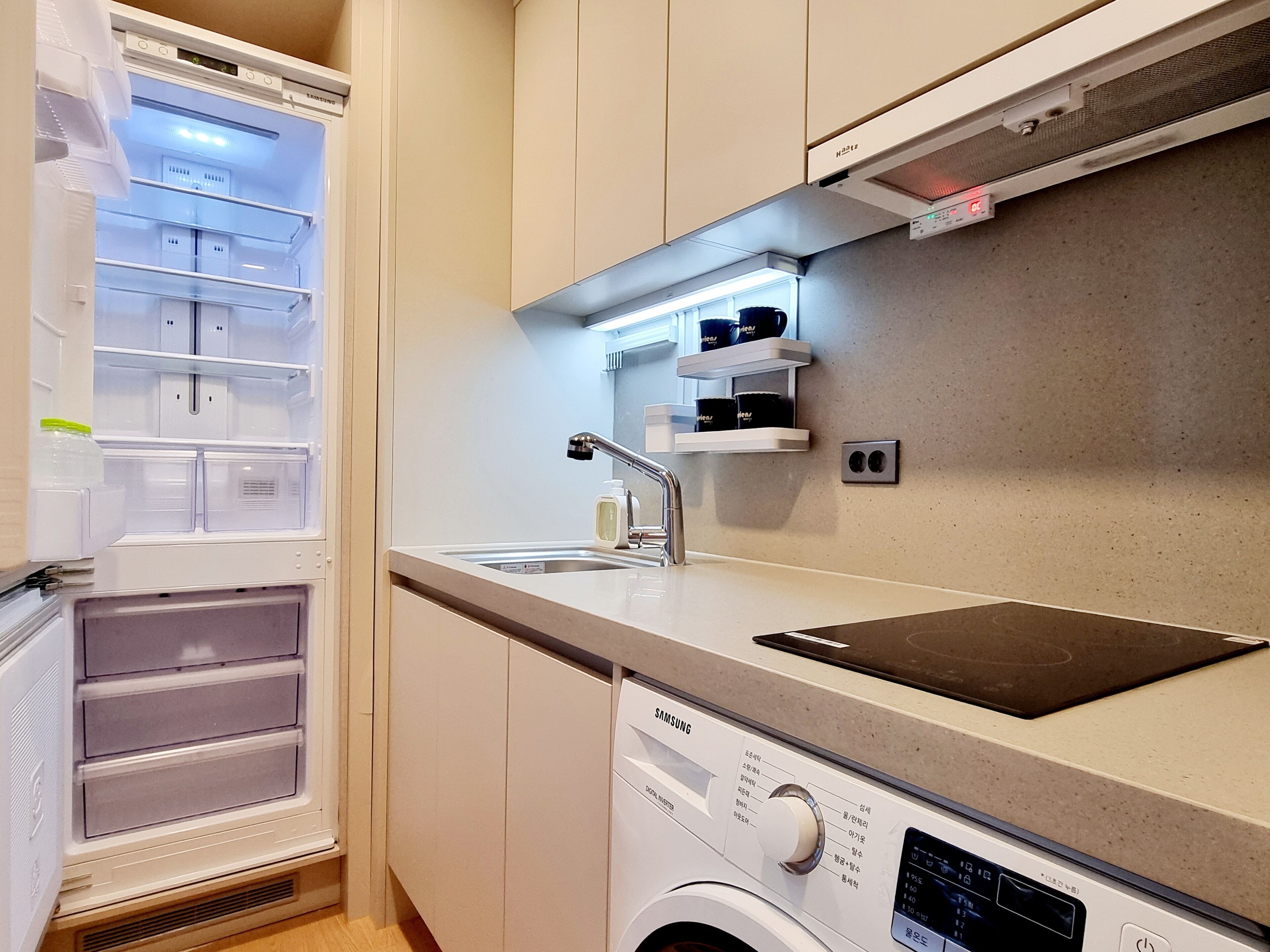 A compact kitchen with a built-in refrigerator, a washing machine, and a sink.